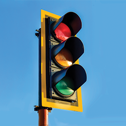 A traffic light with a backplate stands against a blue sky.