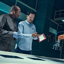 Hai chuyên gia trong nhà máy đang thảo luận về các màn hình thiết bị thông minh được bày trước mặt họ.