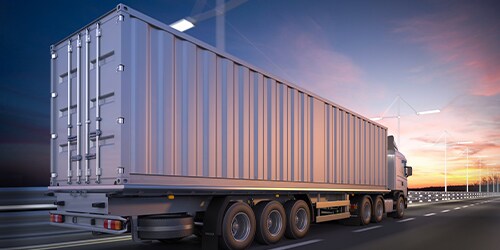 Xe công-ten-nơ hạng nặng chạy trên đường cao tốc dưới bầu trời buổi tối.