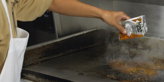 A cook cleans a flat top griddle with the Scotch-Brite Griddle Cleaning System.
