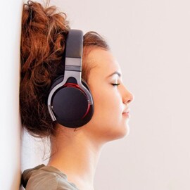 một người phụ nữ tựa vào tường và nghe nhạc với tai nghe không dây chụp tai.