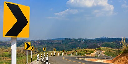 Highly visible road signs indicate a curve in a mountain road.
