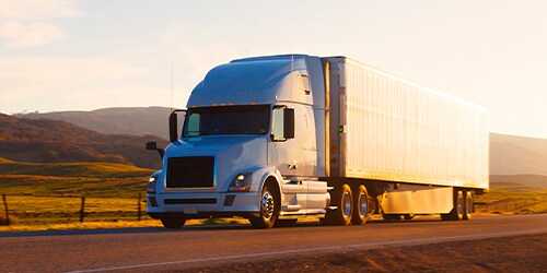 Heavy container vehicle driving along the road against the sunset and hilly background. 
