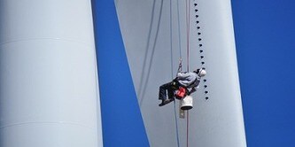 Nhân viên được treo bằng dây an toàn đang kiểm tra cánh tuabin gió.​
