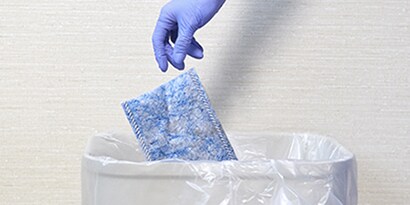 gloved health care cleaning professional disposing of a 3M disposable mop pad
