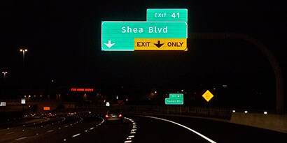 Highway signs are highly reflective over a dark road at nighttime.
