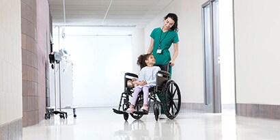 nữ chuyên gia chăm sóc sức khỏe đang đẩy một bệnh nhân trẻ ngồi xe lăn
