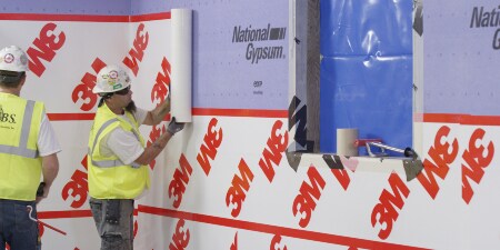 Image of workers installing a 3M™ Air Barrier over drywall and around a flashed wall opening
