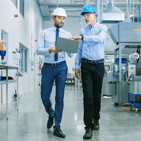 Two men wearing hardhats talking inside a facility