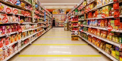 Image of a grocery aisle marked with strips of yellow tape to aid social distancing
