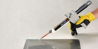 Hình ảnh một công nhân dùng dụng cụ bằng tay để dán keo vào một miếng nhựa
