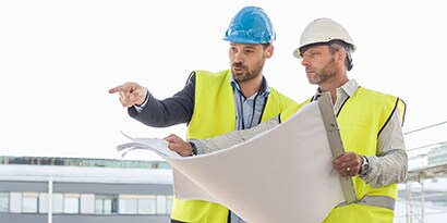 Two workers consult on a job site while reviewing blueprints