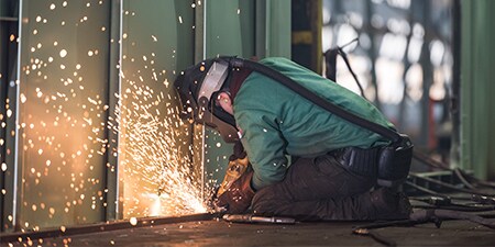 thợ hàn đang mài và đeo mũ hàn với thiết bị lọc và cấp khí

