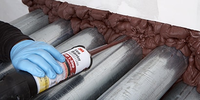 An installer applies 3M™ Fire Barrier Rated Foam FIP 1-Step around pipes in a through-penetration