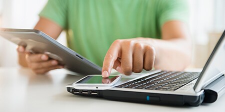 Một người đang cầm máy tính bảng và chạm vào màn hình điện thoại thông minh đặt trên máy tính xách tay.
