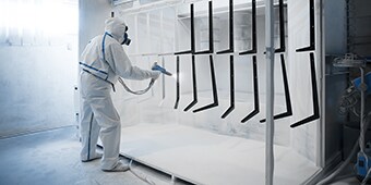 Hình ảnh công nhân mang đồ bảo hộ đang sơn tĩnh điện cho các bộ phận kim loại
