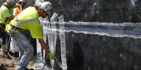 A worker sprays an adhesive before applying the next layer of waterproofing
