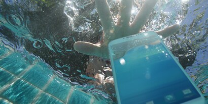 Hand reaching into a pool to grab a phone to show the water resistance of 3M's electronics bonding solutions.
