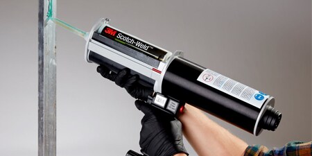 Một công nhân đeo găng sử dụng súng khí nèn để bôi kéo lỏng lên một thanh kim loại thẳng đứng

