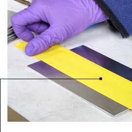 Hình ảnh bàn tay đeo găng đang dán 3M™ Vinyl Tape 471 trước khi xử lý anodizing